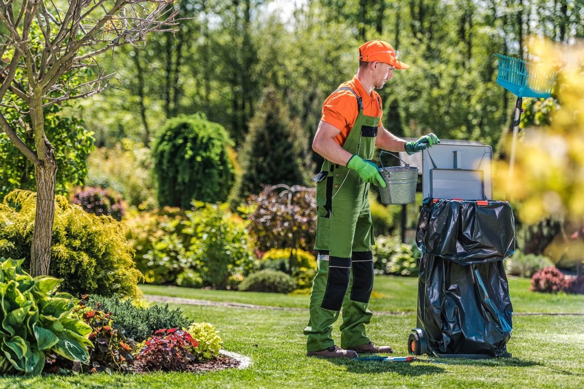 A gardener in bright orange and green attire uses a bucket, working amidst a vibrant and well-maintained garden.